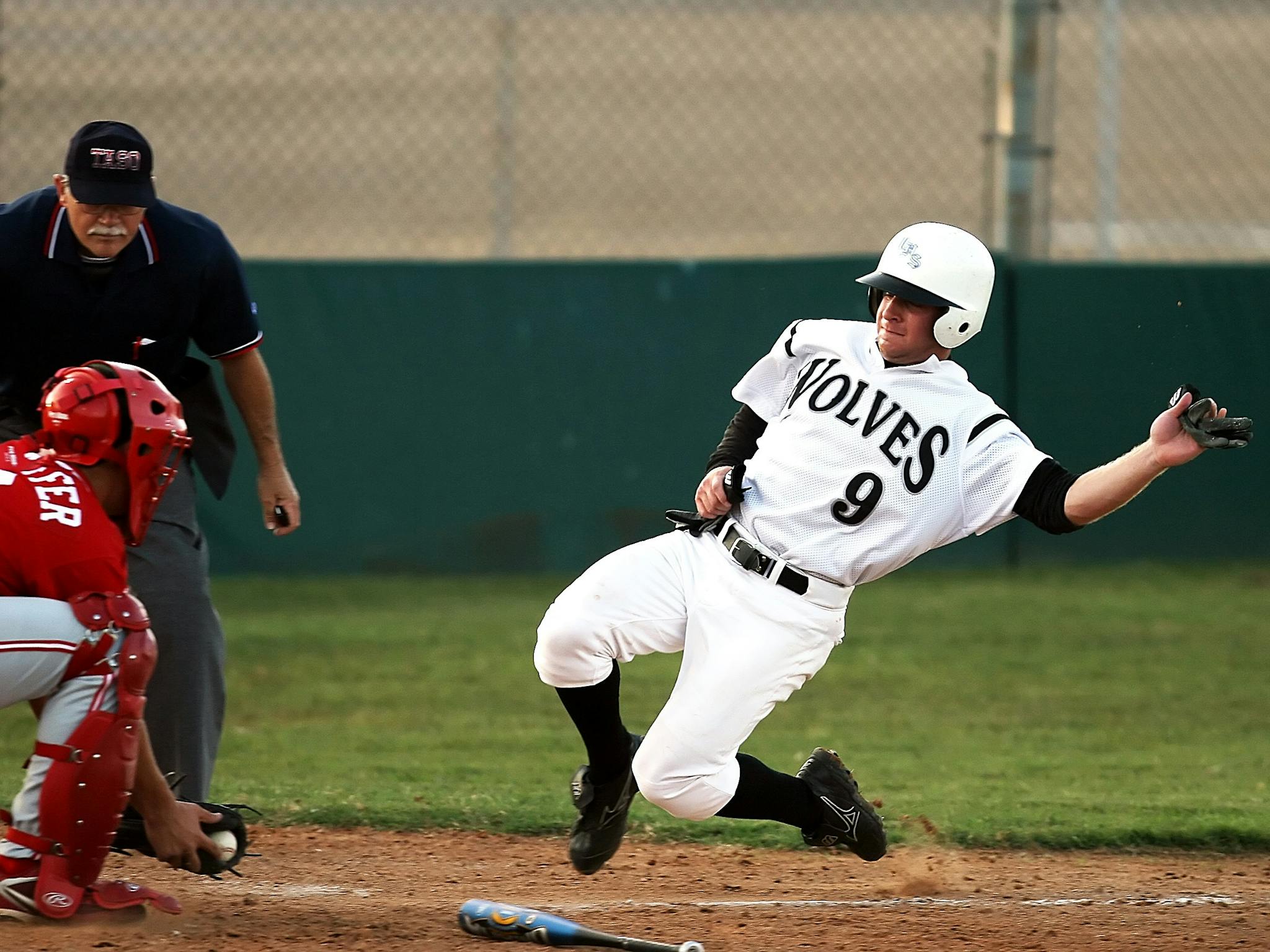 A baseball player wearing a 'wolves' jersey slides into base as the umpire watches intently.