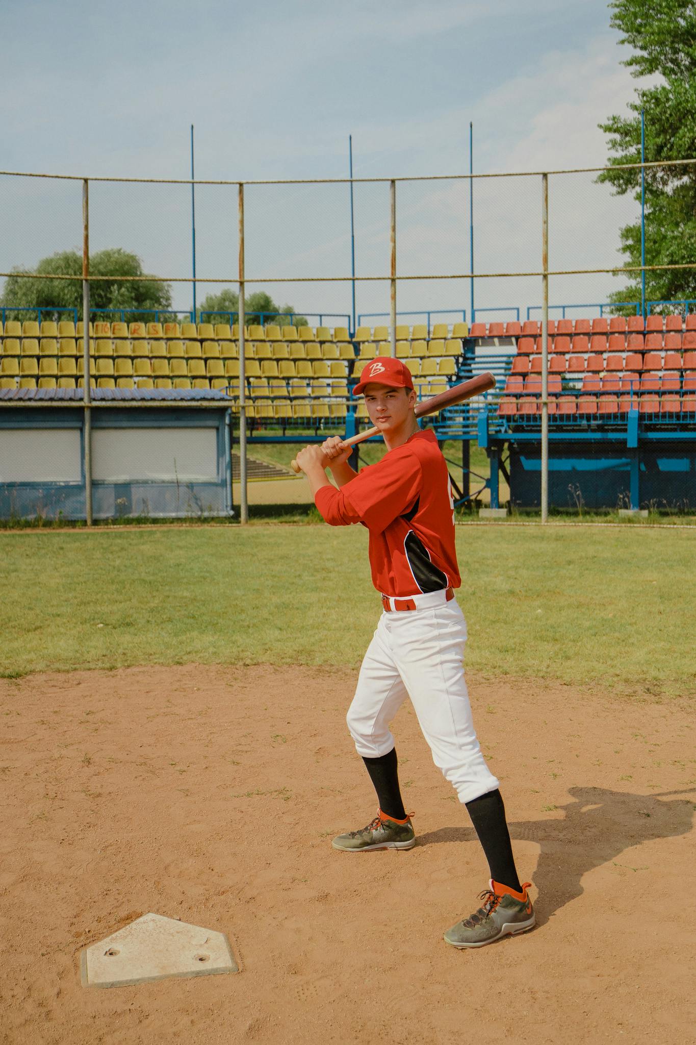 Young baseball player in red uniform prepares to bat on a sunny day at an outdoor stadium.