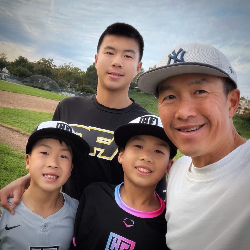 Simon Chan with his 3 boys in travel baseball uniforms on field