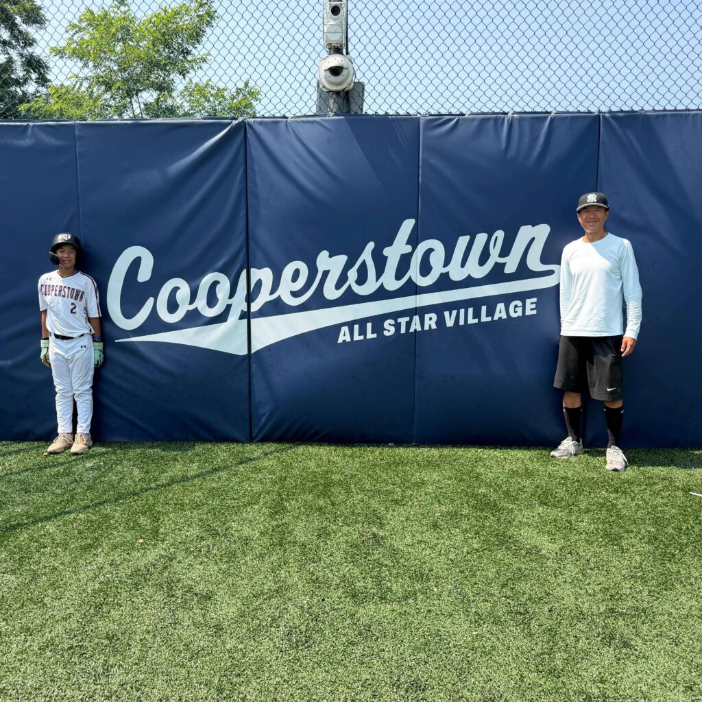 Simon Chan and son next to All Star village logo home plate backdrop 2026