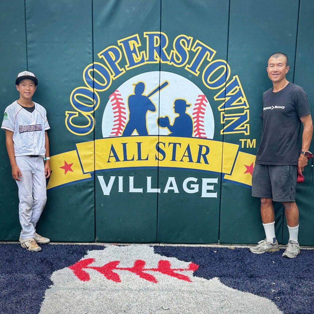 Simon Chan and son next to All Star Village tournament logo home plate backdrop 2023