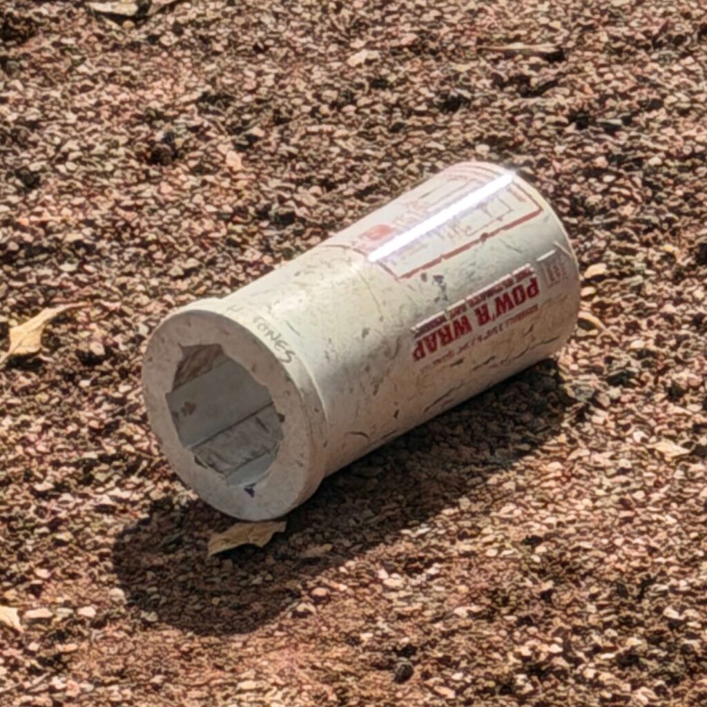 A white Pow'r Wrap baseball bat weight used for on-deck training resting on the ground