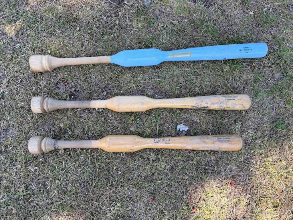 Three wooden hand trainer bats by Camwood and Warstic lying on grass.