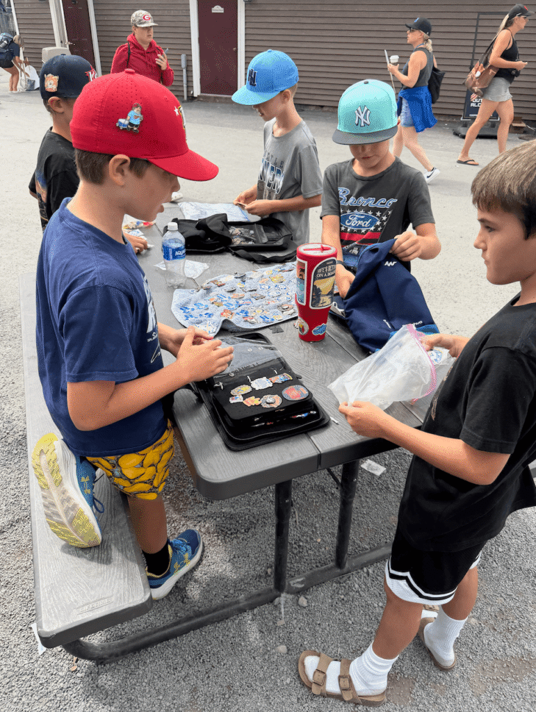 2 kids standing next to table and trading baseball pins