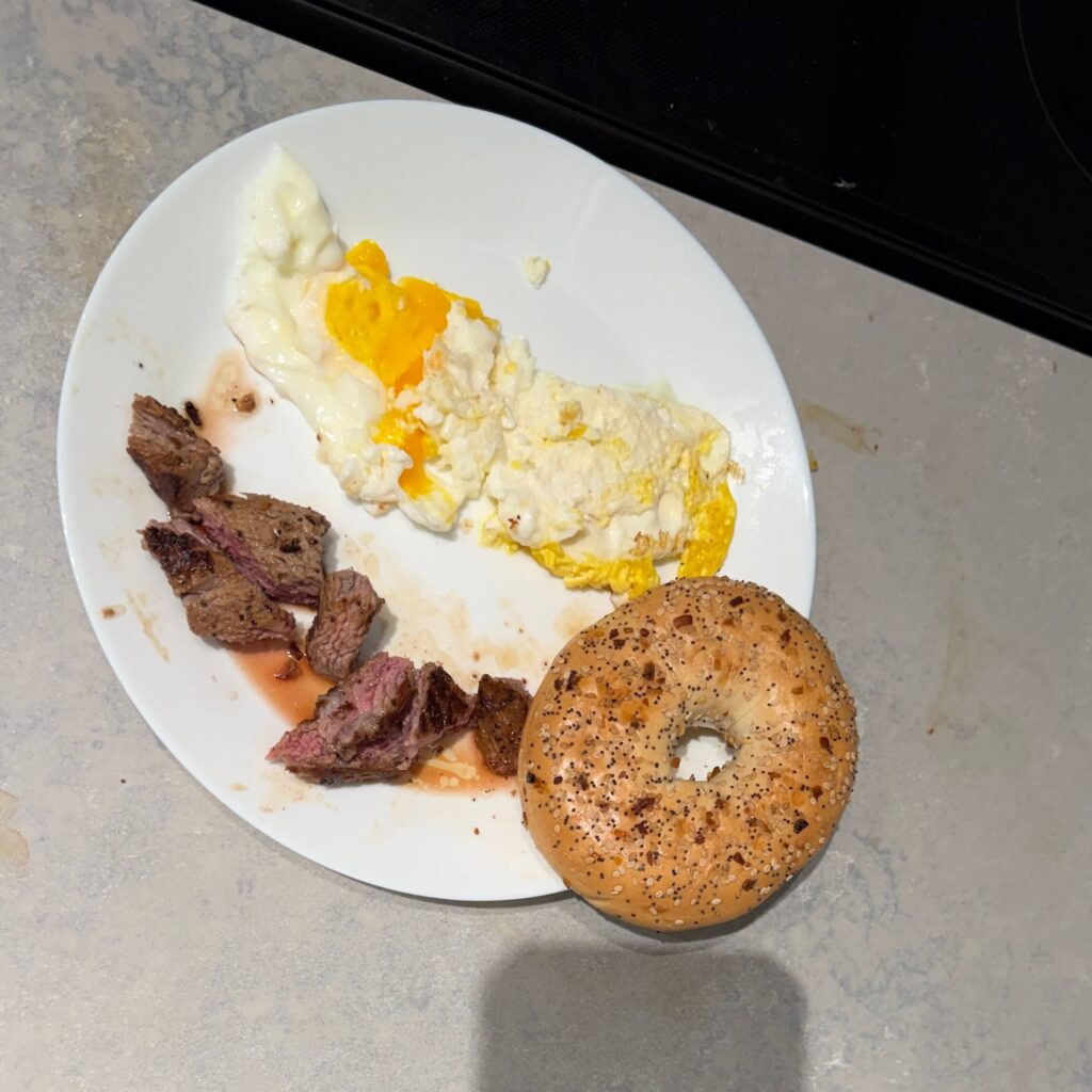plate with sesame bagel, chunks of steak and 2 sunny side up eggs
