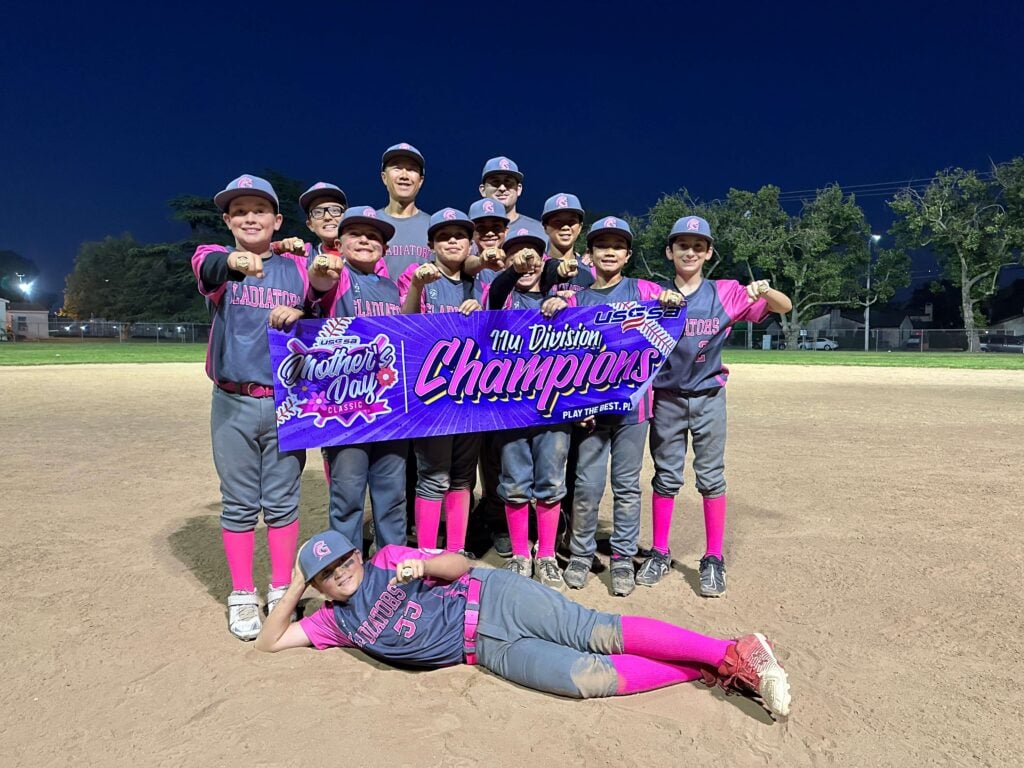 The 11u Gladiators travel baseball team posing on the field at night with their coaches, showing off their championship rings and USSSA Mother's Day Classic Champions banner.