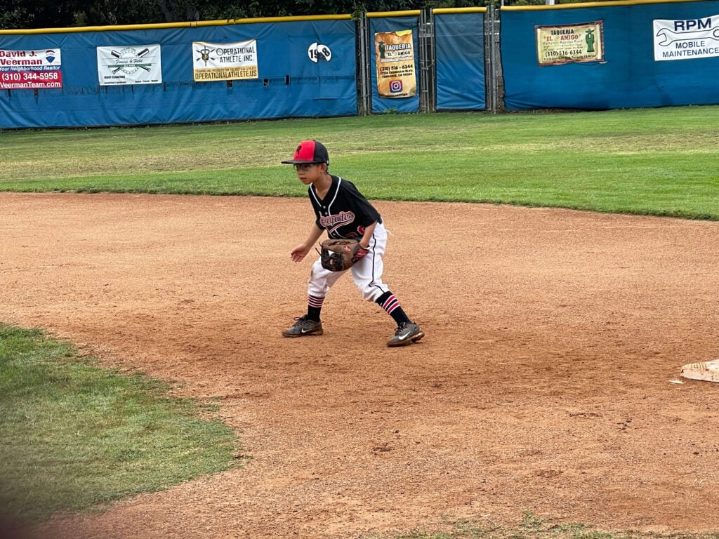 8-year-old travel baseball player in a Renegades uniform in a ready defensive position on the infield dirt during a 9U game