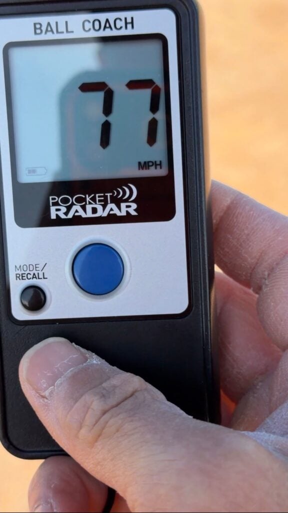 Pocket Radar measuring a 77 mph pitching velocity, representing the elite Majors level for 12U travel baseball.