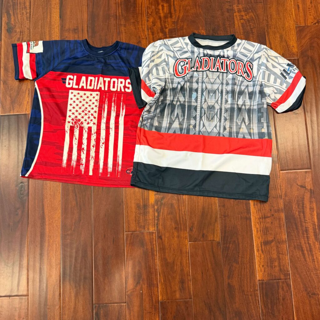 youth travel baseball uniform jerseys from the Gladiators team laid out on a wooden floor, representing the seasonal apparel costs parents pay.